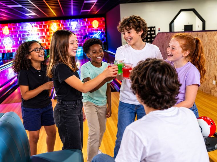 Six enfants trinquent avec leurs boissons au bord des pistes de bowling