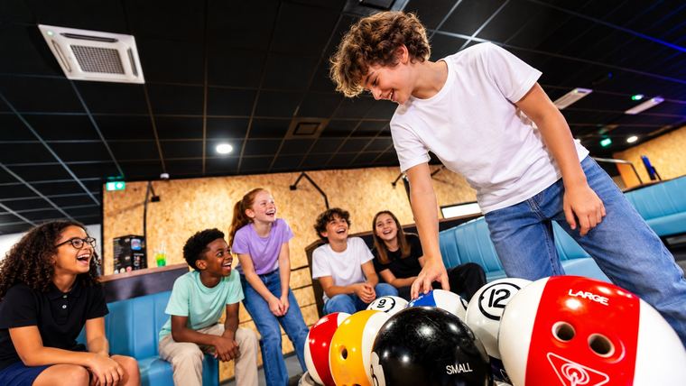 Un enfant choisit sa boule de bowling, ses amis l&rsquo;attendent sur la banquette