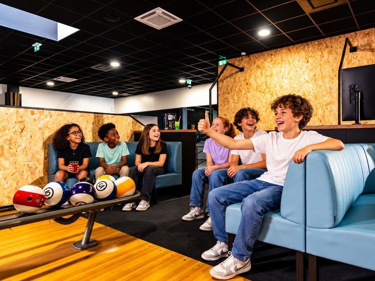 Des enfants assis sur les banquettes du bowling suivent la partie