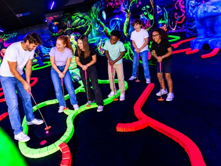 Un parent joue son coup au mini-golf fluo, entouré des enfants du groupe