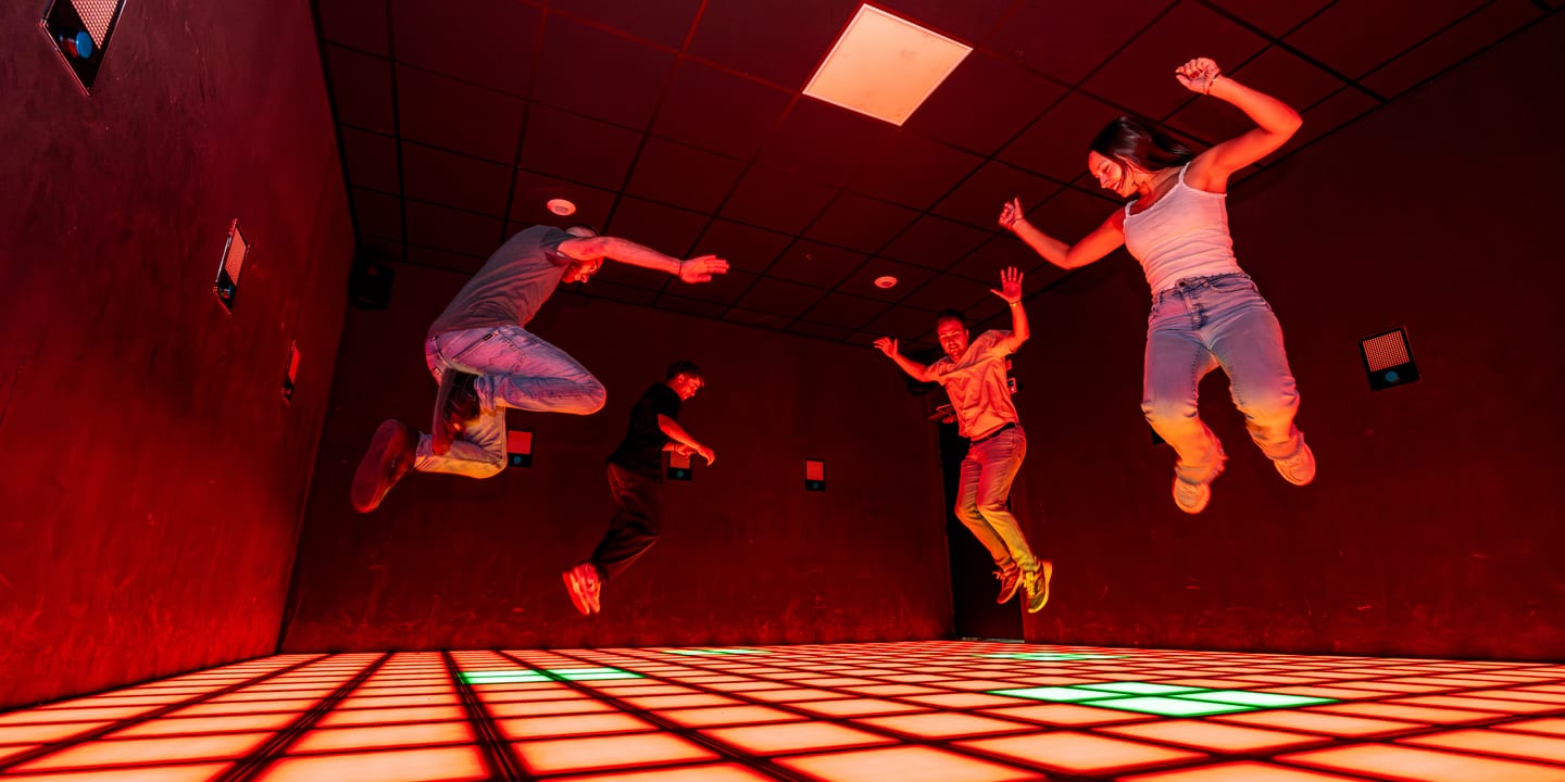 Quatre joueurs en plein saut au-dessus du sol de dalles lumineuses, Pulse UP, jeu floor is lava à Poitiers